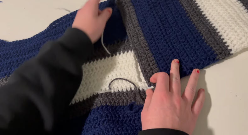 Folding the striped panels to seam the oversized crochet sweater.