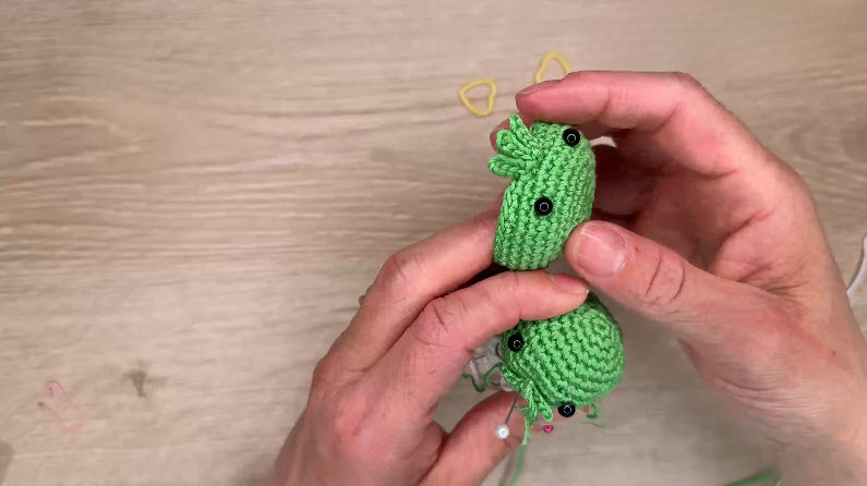 Green amigurumi head with safety eyes, hook inserted