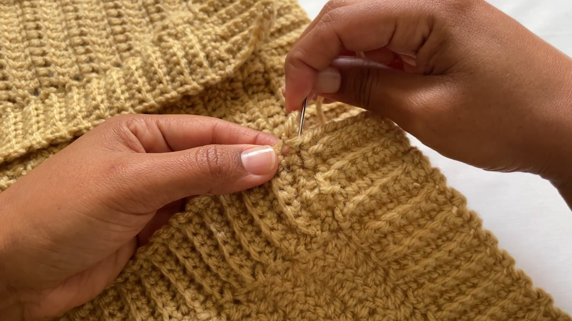 Sewing the cuff seam of the crochet cardigan with a yarn needle.