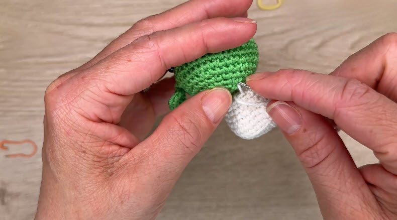White piece being sewn onto green amigurumi body