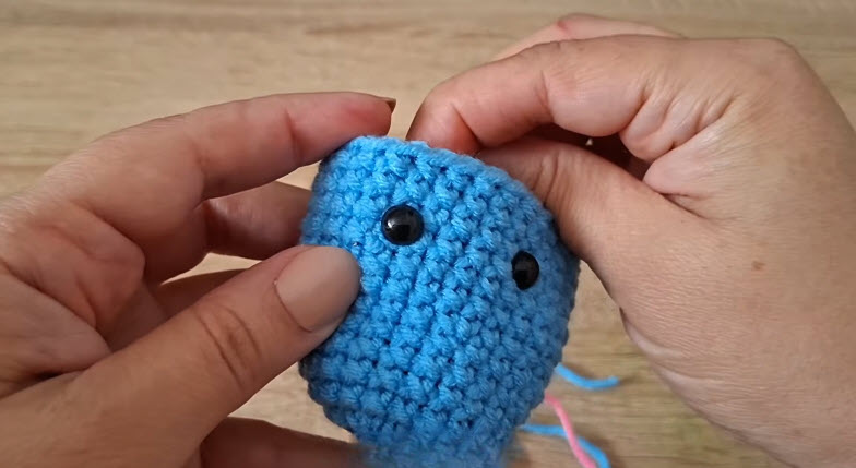 Attaching black safety eyes to a blue crochet dumpling keychain
