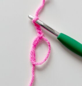 Pink yarn circle with a crochet hook beginning a magic ring